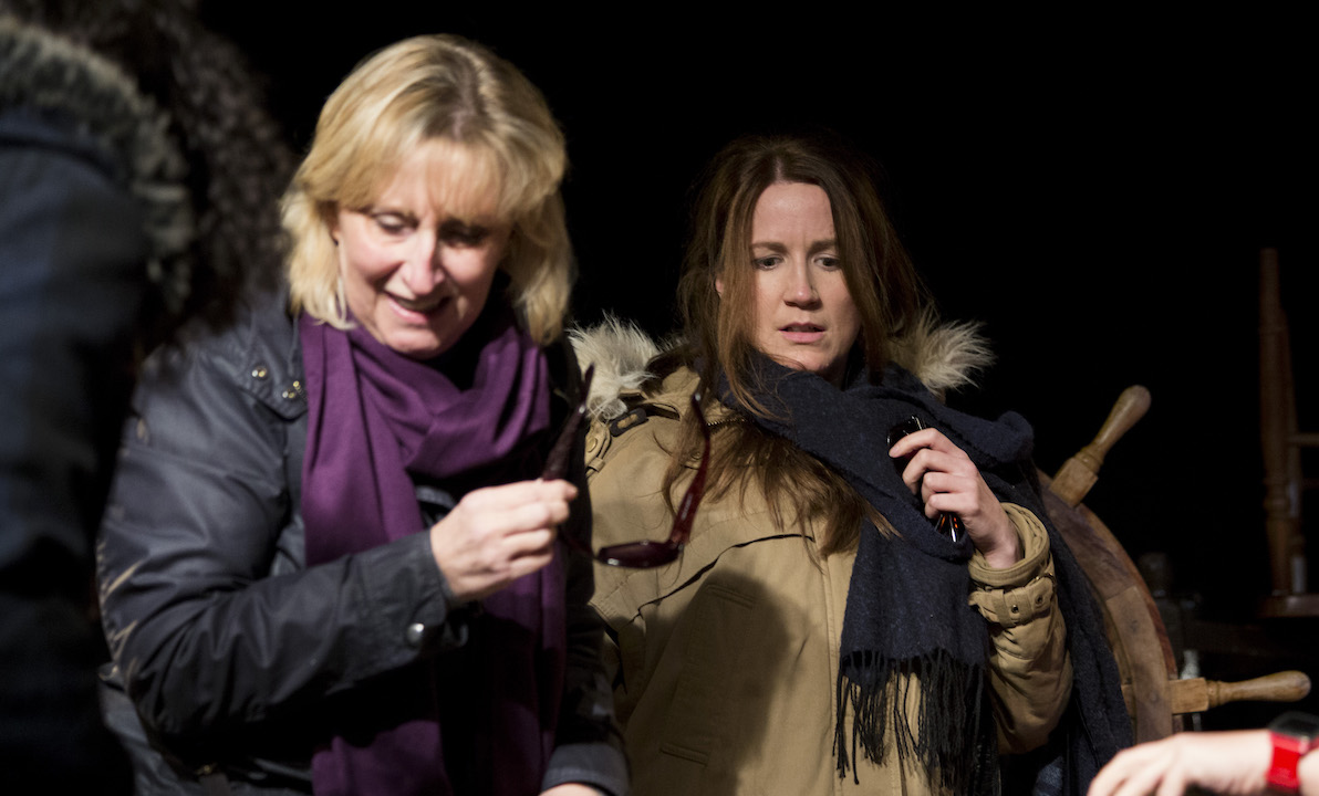 Two women dressed for cold weather, appear to be looking at something low down.