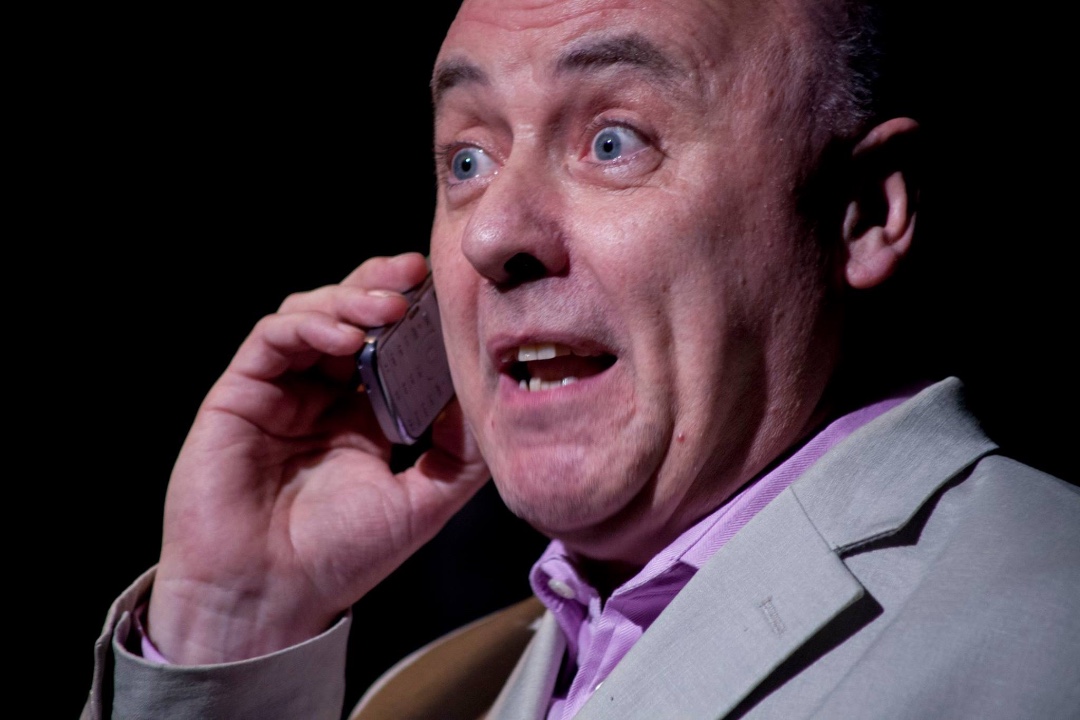 A side on headshot of a man in a purple shirt and grey jacket, with his mobile phone to his ear and a very surprised look on his face.